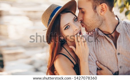 Stylish couple walking outdoors in lawn with a glass of wine. Man and woman looking at each other and walking together outdoors. Sweet kiss.