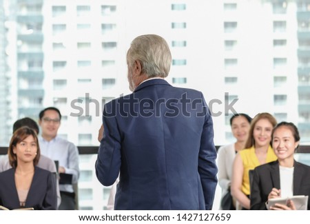 Senior man speaker with blue suit giving a talk to audiences in corporate seminar room. Asian business conferences concept. Light tone.