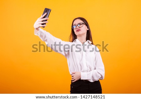 Pretty young girl making a selfie and doing duck lips to the camera in studio over yellow background. Facial expression of young pretty girl.