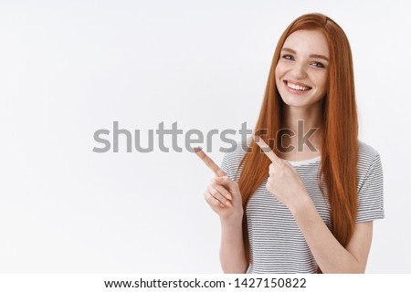 Pleasant pretty redhead young 20s girl blue eyes wearing summer striped t-shirt pointing upper left corner index fingers presenting awesome product advertisement smiling happily, white background