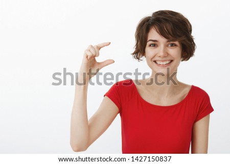 Cheerful happy cute young lucky woman short pixie haircut red t-shirt smiling broadly delighted show hand small tiny little object describe lovely kitten shape stand white background