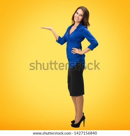 Full body portrait of happy smiling young business woman showing, holding or giving something or copy spase for product or sign text, isolated over orange yellow background