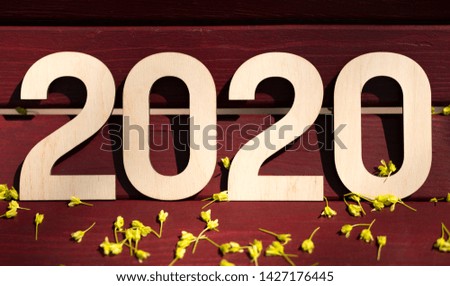 Close up of big 2020 numbers on wooden background with yellow flowers, panorama