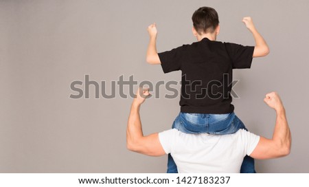 Family of strong men. Muscular man holding his son on shoulders, both showing biceps, gray panorama background with empty space Royalty-Free Stock Photo #1427183237