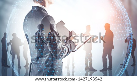 Rear view of businessman with clipboard with his teammates silhouettes and double exposure of planet hologram. Concept of international company and trade. Toned image Royalty-Free Stock Photo #1427193542
