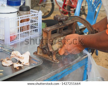 A man crushing dried squids with old machine (only hand in picture), local Thai snacks and street food.