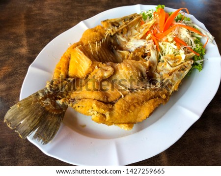 Fried giant perch or snapper fish with sauces (sugar and fish sauces ) in white dish on the table. Taste is sweet and salty.