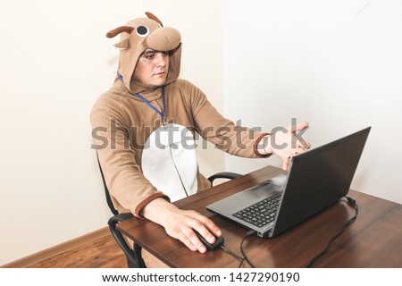 Office worker in cosplay costume of a cow. Guy in the funny animal pyjamas sleepwear near the laptop. Parody on manager.