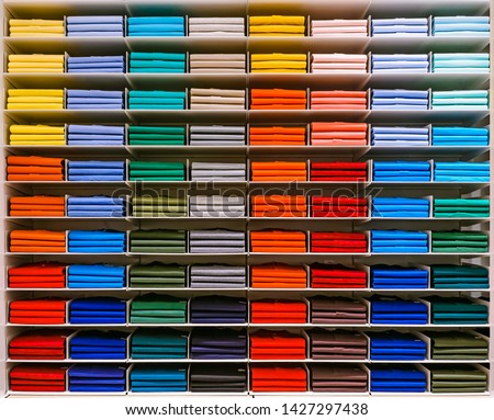 Colorful rainbow clothes background .Various vibrant color shirts perfectly folded on a shelf in the shop. Colored male clothes displayed in store. T-shirt of different color are neatly stacked in a Royalty-Free Stock Photo #1427297438