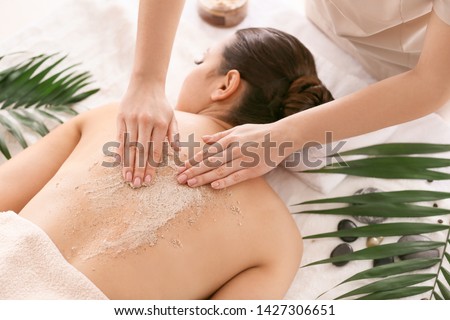 Young woman undergoing treatment with body scrub in spa salon Royalty-Free Stock Photo #1427306651