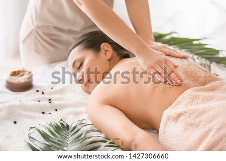 Young woman undergoing treatment with body scrub in spa salon Royalty-Free Stock Photo #1427306660