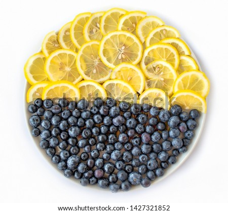 Bueberries and lemon on a round plate on a white background. Top view. Geometric view of berries and fruits on a plate.