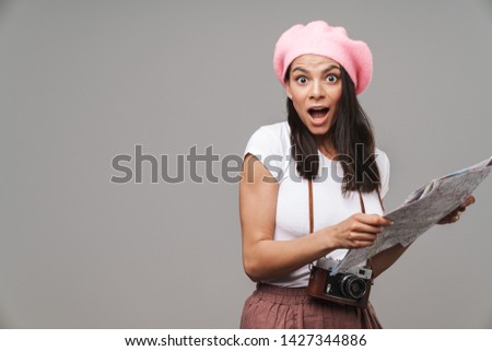 Image closeup of surprised young tourist woman with retro vintage camera wondering and holding paper map isolated over gray background