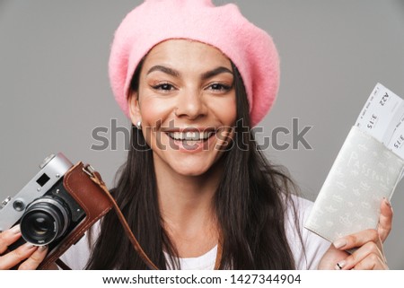 Photo closeup of gorgeous pretty tourist woman in beret smiling while holding retro camera and travel tickets isolated over gray background