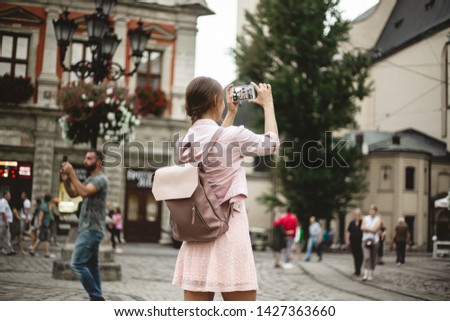 Hipster girl with backpack holds smartphone. Traveler photographs the cityscape at sunset. Lifestyle