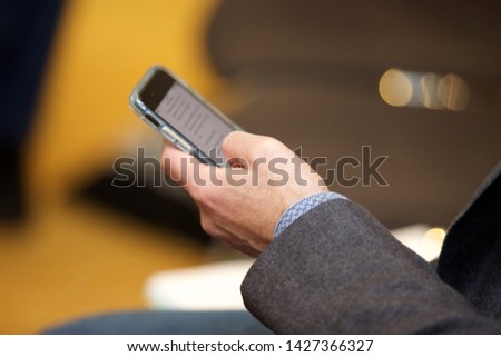 Businessman at a conference or seminar browsing the internet on his mobile phone.