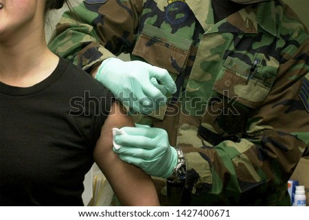 Military doctor vaccinating a female soldier. Royalty-Free Stock Photo #1427400671