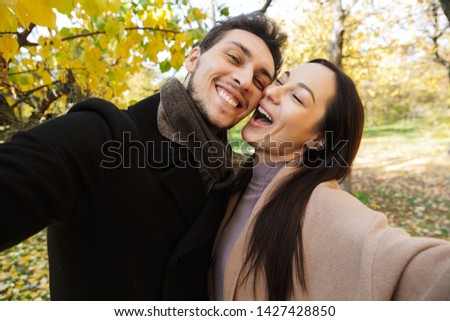 Beautiful young couple in love spending time together at the park in autumn, taking a selfie, hugging