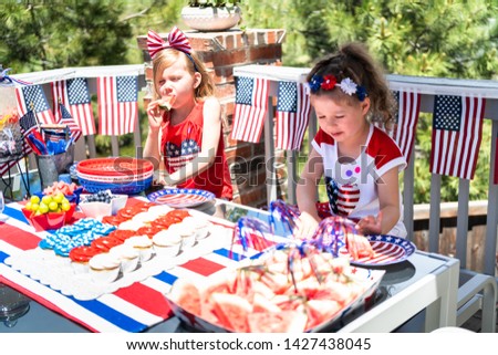 Little girls are playing at the July 4th party on the back patio.
