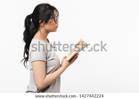 Photo of asian thoughtful beautiful young woman posing isolated over white wall background holding book reading.