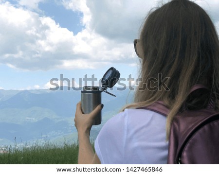 Young woman-traveler drinking tea from a thermo mug across mountains landscape. Copy space