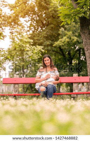 A beautiful mother sitting on a bench in the park and feeding her baby girl in her arms.