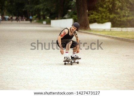 Skateboarder doing a trick at the city's street in cloudly day. Young man in sneakers and cap riding and longboarding on the asphalt. Concept of leisure activity, sport, extreme, hobby and motion.