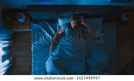Top View of a Young Man in Bed at Night Having Terrible Nightmare, He Wakes Up Scared and Covered in Sweat. Royalty-Free Stock Photo #1427499947
