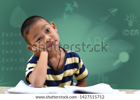 Smart boy asia is doing homework, he is thinking over a difficult task. The portrait against blackboard background. Concept learning in elementary school