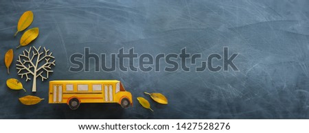 education and back to school. Top view photo of cardboard bus next to autumn dry leaves over classroom blackboard background