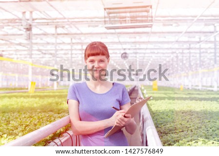 Portrait of young female botanist standing with clipboard in plant nursery