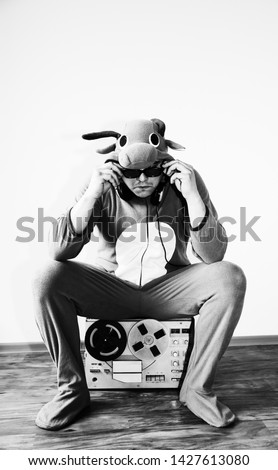 Man in cosplay costume of a cow with reel tape recorder. Guy in the animal pyjamas sleepwear. Funny photo with party ideas. Disco retro music.