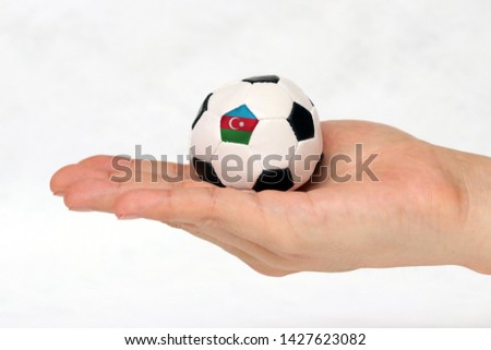 Mini football in hand and one black point of football is Azerbaijan flag on white background. Concept of sport or the game in handle.