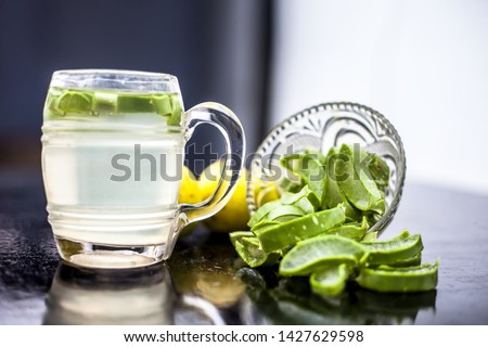 Close up of glass mug on wooden surface containing aloe vera and lemon juice detox drink along with its entire raw ingredients with it. Horizontal shot with blurred background.
