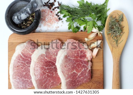 Large pieces of fresh pork on a cutting board, pink salt, cloves, allspice in a mortar, spicy herbs, top view,  close-up on a white background.