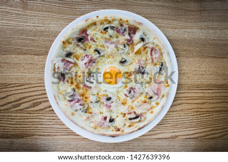 Italian meat pizza with egg, on a white plate and wooden background