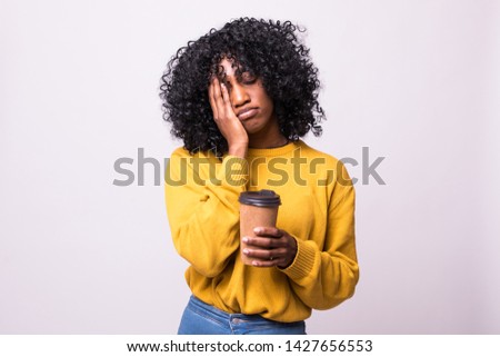Only coffee may refresh me. Tired sleepy ethnic woman covers half of face with palm, has sad expression, closes eyes, carries disposable cup of drink containing caffeine, has continue working
