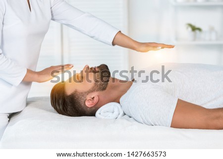 cropped view of healer putting hands above head while healing handsome man on massage table Royalty-Free Stock Photo #1427663573