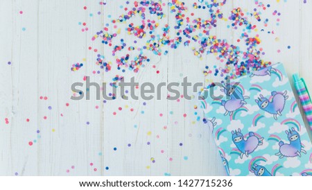 Notebook with llama unicorn and rainbow with colorful gel pen on white wooden background with confetti. Idea of Girly Desk table