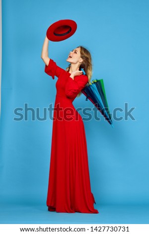   woman in a long dress with an umbrella is looking at the hat on a blue background                            