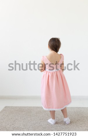 Rear view of a charming little girl princess in a pink dress posing in a designer dress on a white background. The concept of children's clothes. Copy space