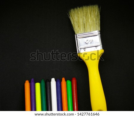 A set of creative materials on the desktop, paint brush and multi-colored crayons for creative work on a black wooden table, a blank background with a pattern, space for copies, flat lay