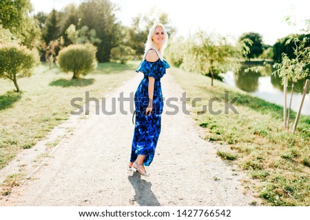 Beautiful blonde girl posing at nature in blue dress