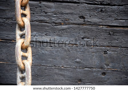 Rusty anchor chain on the background of an old wooden decorative ship. The surface is covered with black lacquer. Selective focus. Copy space.