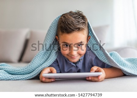 Portrait of a young child at home watching cartoon on the tablet PC. Modern kid and education technology. Portrait of a satisfied cute little kid playing games on tablet computer