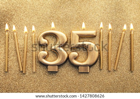 Number 35 gold celebration candle on a glitter background