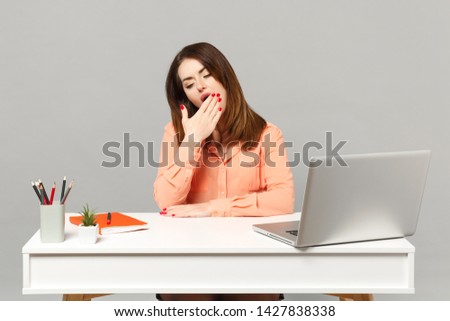 Young tired woman in pastel casual clothes yawning, covering mouth with hand work at desk with pc laptop isolated on gray background. Achievement business career lifestyle concept. Mock up copy space
