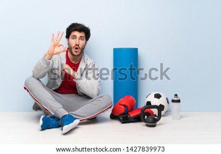 Sport man sitting on the floor surprised and showing ok sign