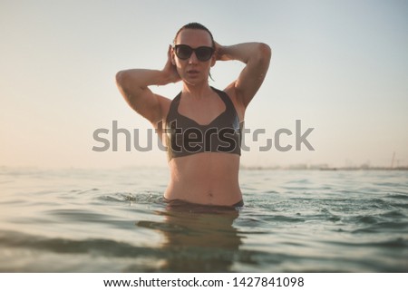 Slim lady posing in sunglasses and latex bra standing in the sea