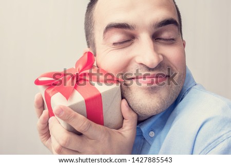 An attractive man received a gift for his birthday. The man is happy and closed his eyes in pleasure. Portrait, close up, toned